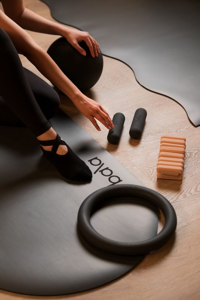 Woman sitting on Pilates mat with ring, weights, and ball